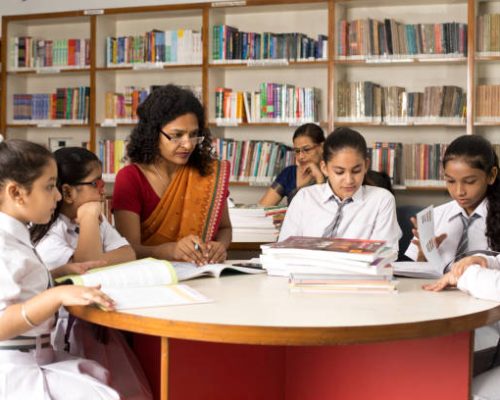 Female teachers teaching students in library at school